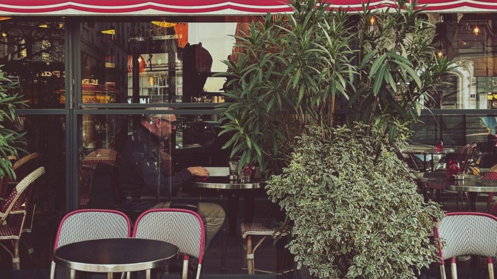 "Intérieur d'un café parisien avec un client assis à une table,entouré de plantes et de chaises de terrace.En 2025,la tarification des collaborations avec des influenceurs sur Snapchat en France devient un facteur clé pour les entreprises cherchant à optimiser leur stratégie de marketing digital et à atteindre un public plus large."