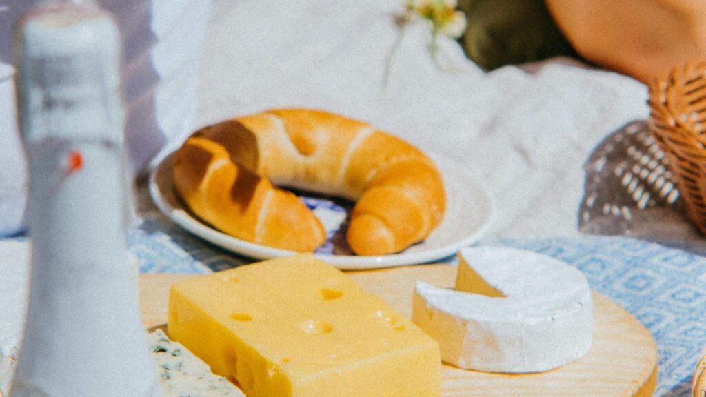 Un délicieux assortiment de fromages, y compris un fromage à trous, un camembert avec une part enlevée, et un croissant doré sur une assiette. Cette image est associée aux Tarifs des Collaborations avec des Influenceurs sur Twitter en France en 2025.