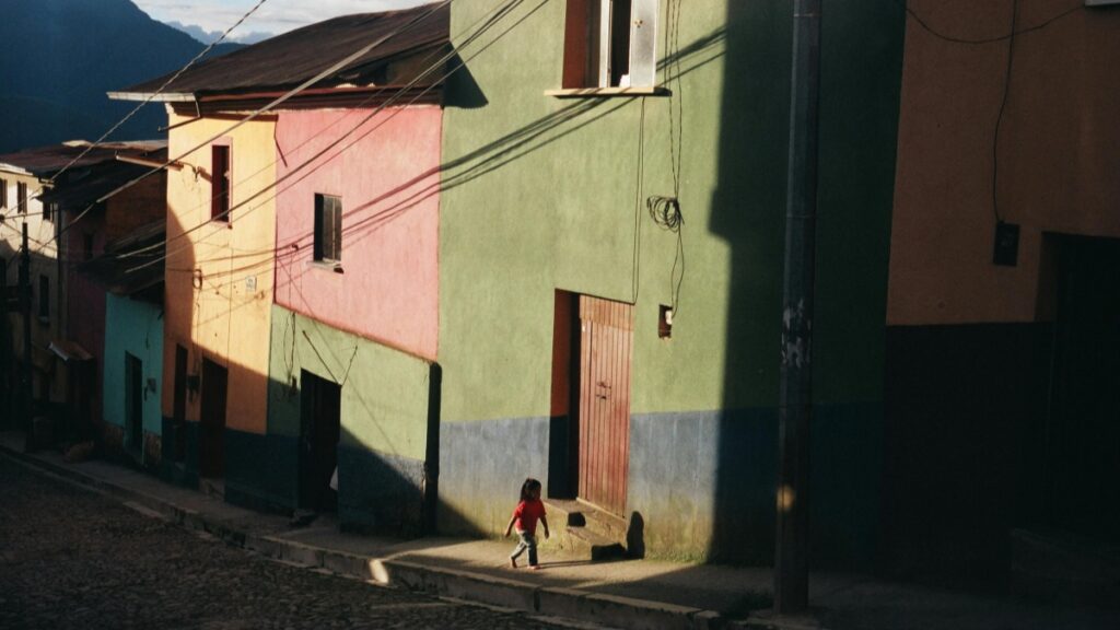 Une rue pavée avec des maisons colorées, telles que des murs en vert, rose et jaune, et des fils électriques partout. Un enfant en rouge marche sur le trottoir. Cette image est associée aux Tarifs des Collaborations avec des Influenceurs sur Viber en France en 2025.