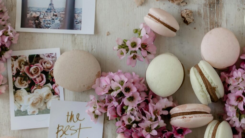 Un arrangement appétissant de macarons en différentes nuances, tels que le rose et le blanc, entourés de fleurs roses. Avec des photos, dont une de la Tour Eiffel, et une carte qui dit "the best". Cette image est associée aux Tarifs des Collaborations avec des Influenceurs sur Vigo Video en France en 2025.
