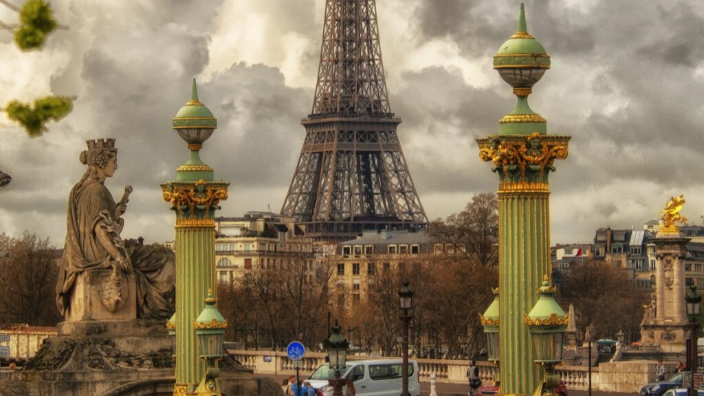 Une vue emblématique de la Tour Eiffel à Paris, avec des colonnes ornées de vert et d'or et une statue en toile de fond. Le ciel est couvert de nuages. Cette image est associée aux Tarifs des Collaborations avec des Influenceurs sur WeChat en France en 2025.