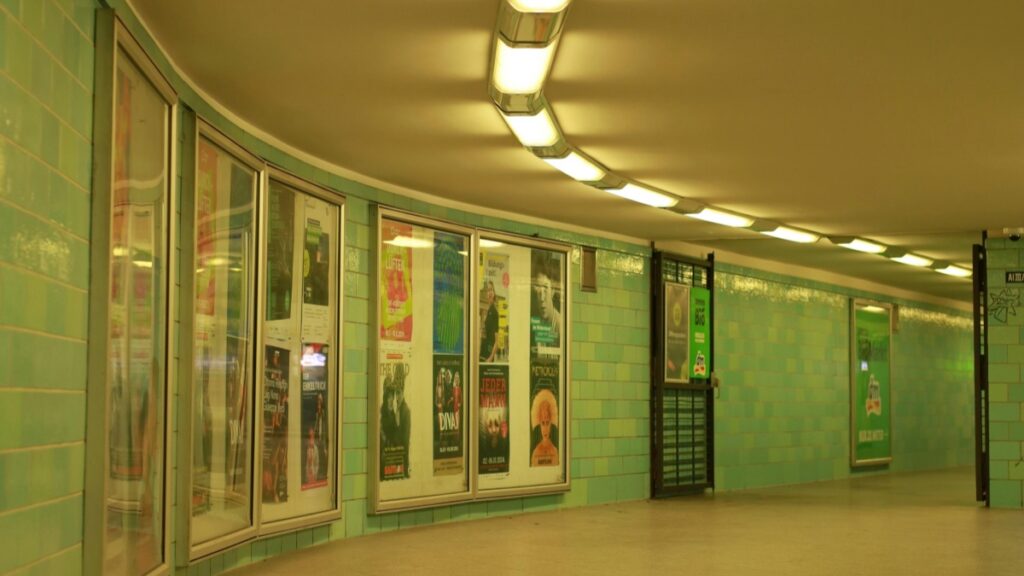 Dieses Bild zeigt einen Unterpass mit einer grünlichen Wand, auf der mehrere Plakate in Schaukästen aufbewahrt sind. Die Decke ist mit einer Reihe von Leuchten ausgestattet, die das Gebiet beleuchten. Wer sich für Alternativen zu TikTok interessiert, sollte sich "Vigo Video Der unbekannte Verwandte von TikTok" näher ansehen, um mehr über diese Plattform zu erfahren.