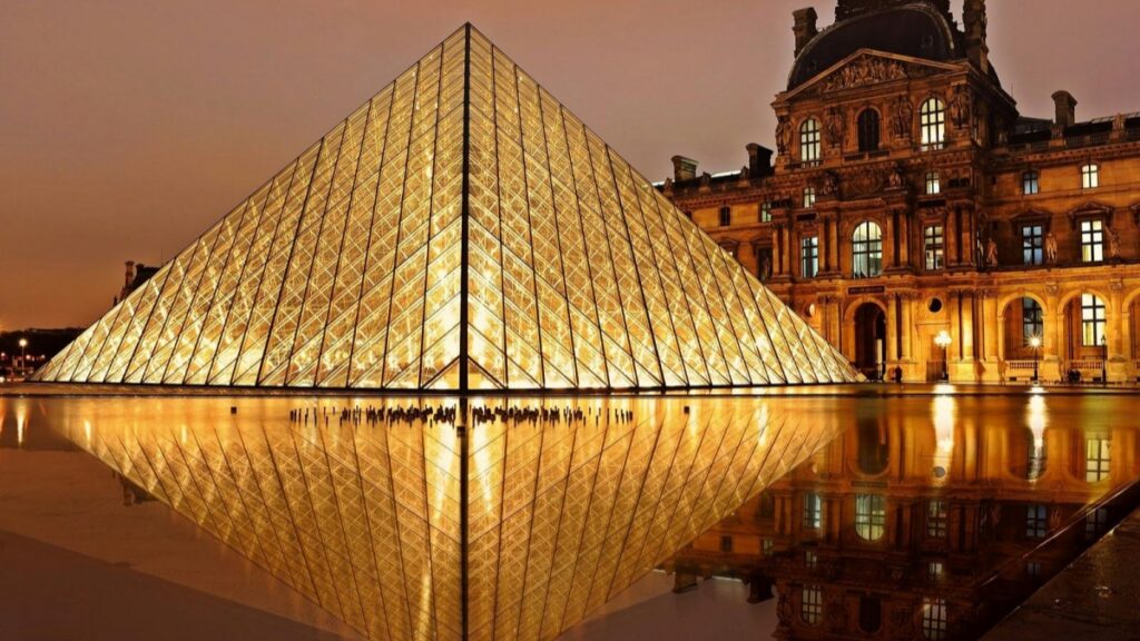 Cette image montre la célèbre pyramide en verre du Musée du Louvre à Paris, illuminée la nuit, avec sa réflexion dans l'eau. À côté se trouve l'édifice historique du Louvre, orné de détails architecturaux élégants. Pour ceux intéressés par les plateformes de partage de vidéos, découvrir "Vigo Video Le cousin méconnu de TikTok" peut apporter des informations précieuses sur les alternatives au monde de TikTok.