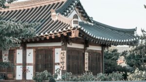 전통적인 한국집이 있습니다. 기와屋顶가 뚜렷하고, 나무와 흰 벽으로 구성된 외관이 특징적입니다. 문과 창에 격자 디자인이 있으며, 옆에 한국어 글씨가 쓴 판이 걸려 있습니다. 주변에는 나무들이 둘러싸여 자연스러운 분위기를 연출합니다. WhatsApp으로 돈 벌기 실용적인 팁에 대해 더 알아보세요.