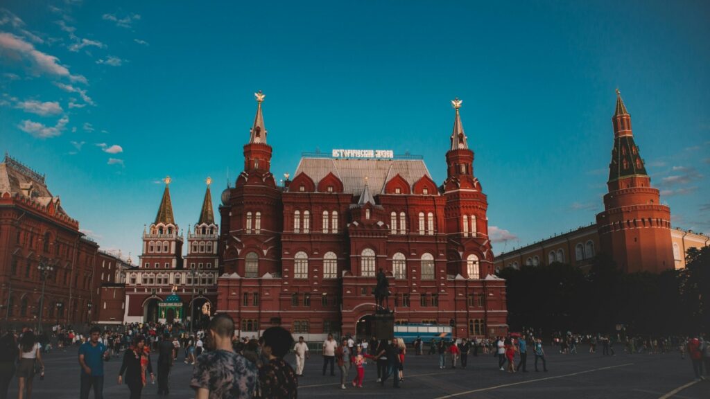This image captures the grandeur of the State Historical Museum in Moscow, Russia, with its distinctive red brick architecture and ornate spires against a clear blue sky. The bustling square in front is filled with people, adding a lively atmosphere to the scene. For Russians interested in learning how to monetize their presence on Twitter, the guide "Как зарабатывать деньги в Twitter: Практическое руководство для россиян" offers valuable insights.