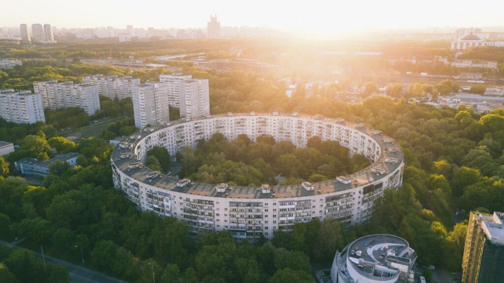 Вид с высоты на круговой многоквартирный дом, окруженный зеленью. В.Background - другие дома и города, окутанные рассветным или закатным светом. Эта панорама иллюстрирует современный городской образ жизни. Узнайте, Как использовать WeChat для маркетинга бизнеса в Росси.