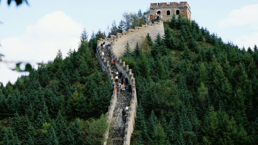 这张图片展示了雄伟的中国长城，蜿蜒在郁郁葱葱的山林间，许多游客正在攀登。长城作为世界文化遗产，承载着厚重的历史。此外，若你想了解在中国如何利用微信进行商业营销，可获取相关策略与技巧，助力拓展商业版图。
