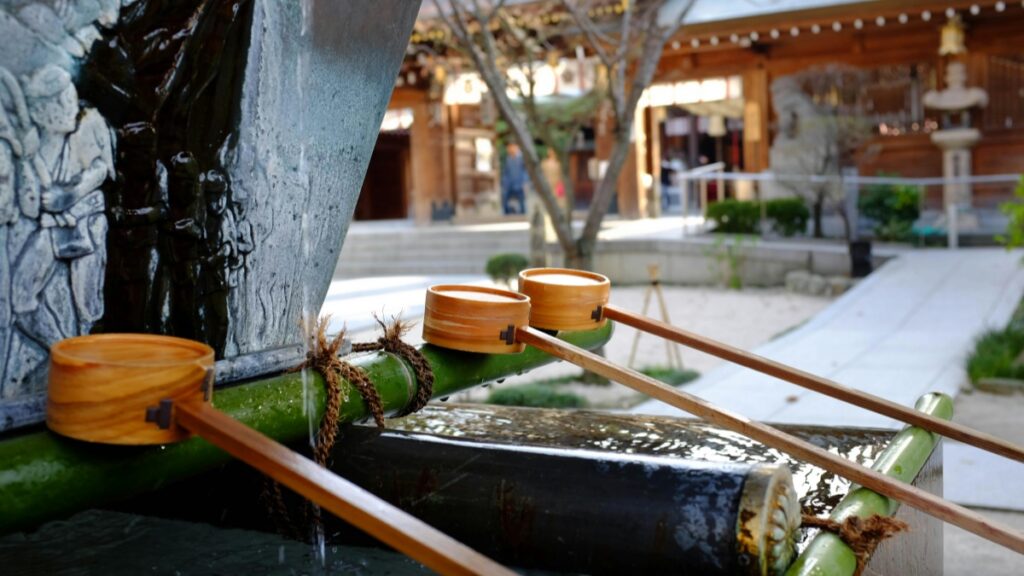 この写真は、伝統的な日本の神社風景を展示しています。竹の注水装置が静かに水を石製の池に注いでいます。背景には神社の建物や参拝者も見えます。2025年の日本iMessageインフルエンサー推奨協力料金基準とは、iMessageプラットフォームを通じて活動するSNSインフルエンサーとの協力費用の推奨基準です。これにより、インフルエンサーとの協力がより規範化され、促進されます。